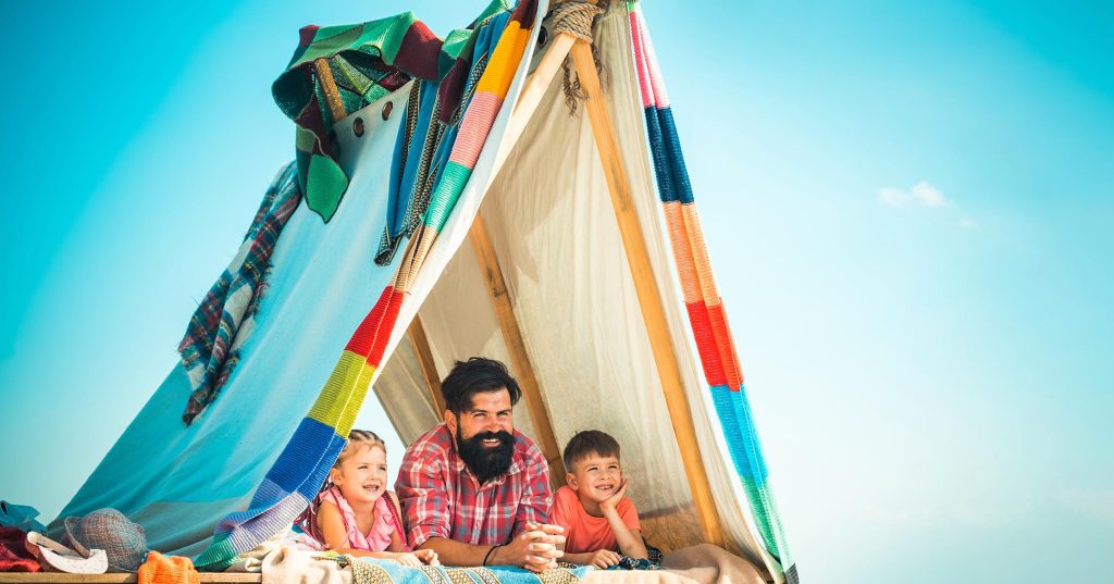Itse kyhätyssä teltassa isä ja kaksi lasta katselevat taivaalle ja hymyilevät.