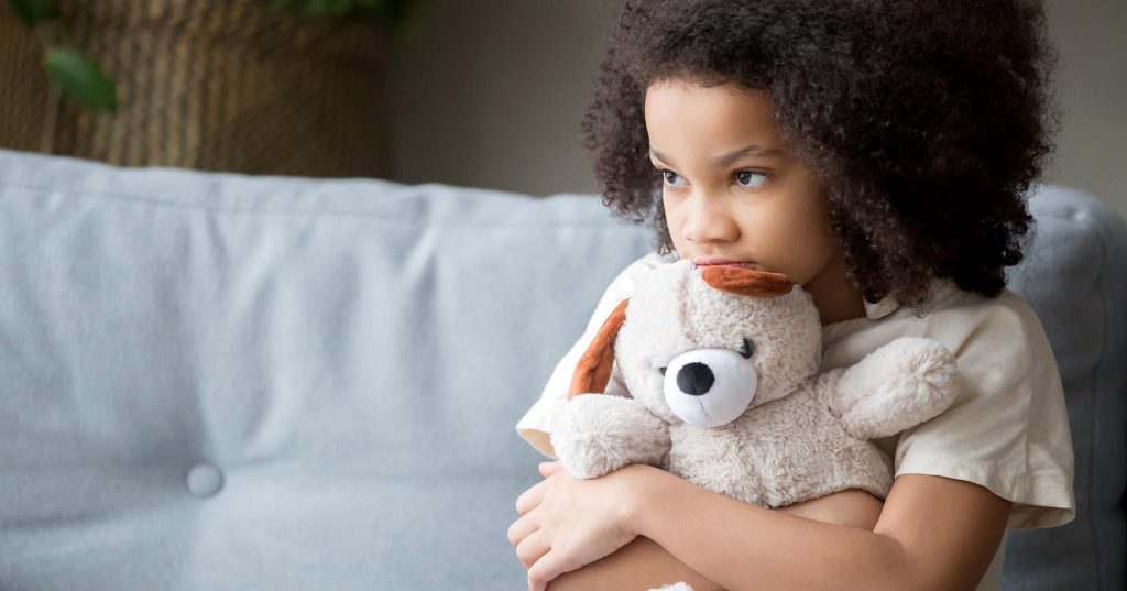 Tyttö rutistaa pehmolelua sohvalla istuen.