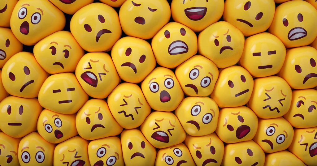 Paljon emojin näköisiä palloja lytättynä tiiviseen tilaan tukalaan paineeseen, jokaisella eri tunne kasvoilla.