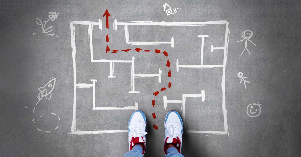 Jalat lenkkitoissuissa ovat astumassa maahan piirrettyyn labyrinttiin, johon on merkitty reitti ulos.