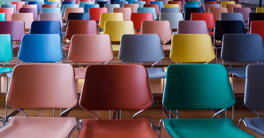 Erivärisiä tyhjiä tuoleja salissa.