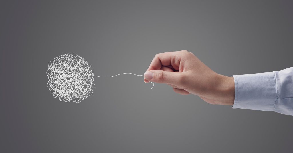 Virkamiesmäinen käsi kurottaa ilmassa kohti lankakerää ja alkaa vetää vyyhtiä auki langan päästä.