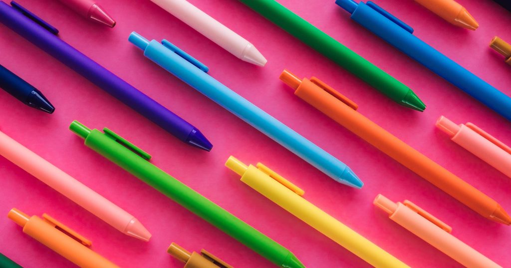 Värikkäitä kyniä pinkillä pöydällä.