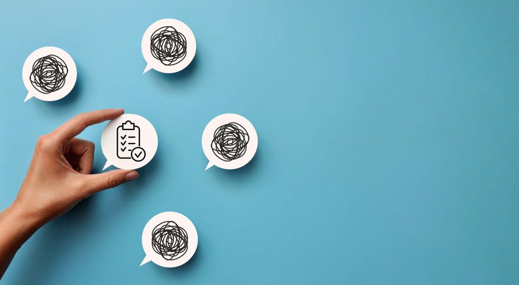 Käsi asettelee seinälle puhekuplaa, jossa asiat ovat luettelona järjestyksessä. Seinällä on jo useita puhekuplia, joissa on vain suttua.